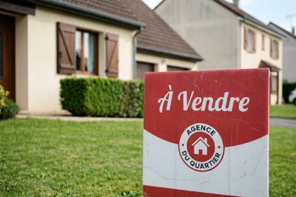 Panneau immobilier 'À Vendre' planté devant une maison individuelle dans un quartier résidentiel